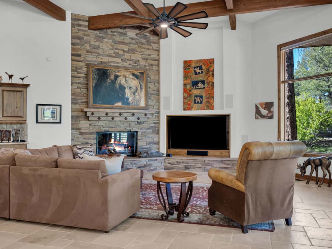 14 of 52. Inviting living room with floor-to-ceiling stone fireplace, custom built-ins, expansive windows, and comfortable seating areas overlooking the beautiful forest setting.