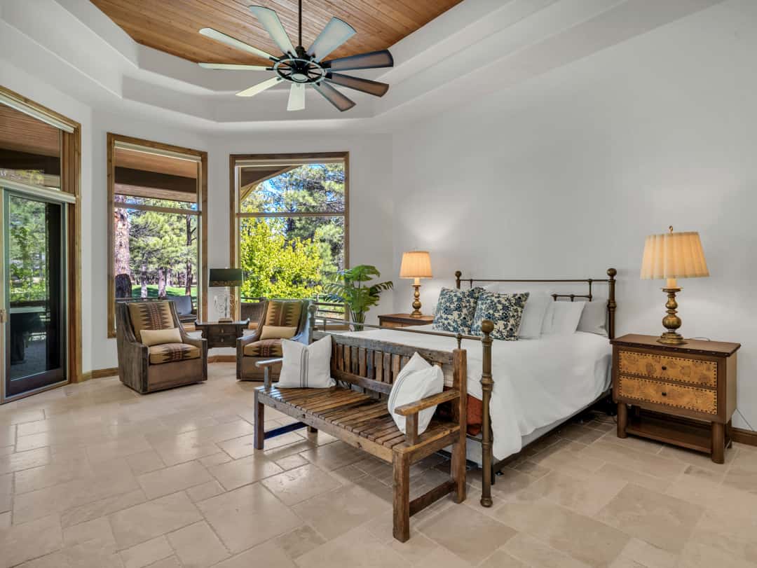 16 of 52. Spacious primary suite with vaulted ceilings, large windows, outdoor patio access, and serene pine forest views designed for luxury mountain living.