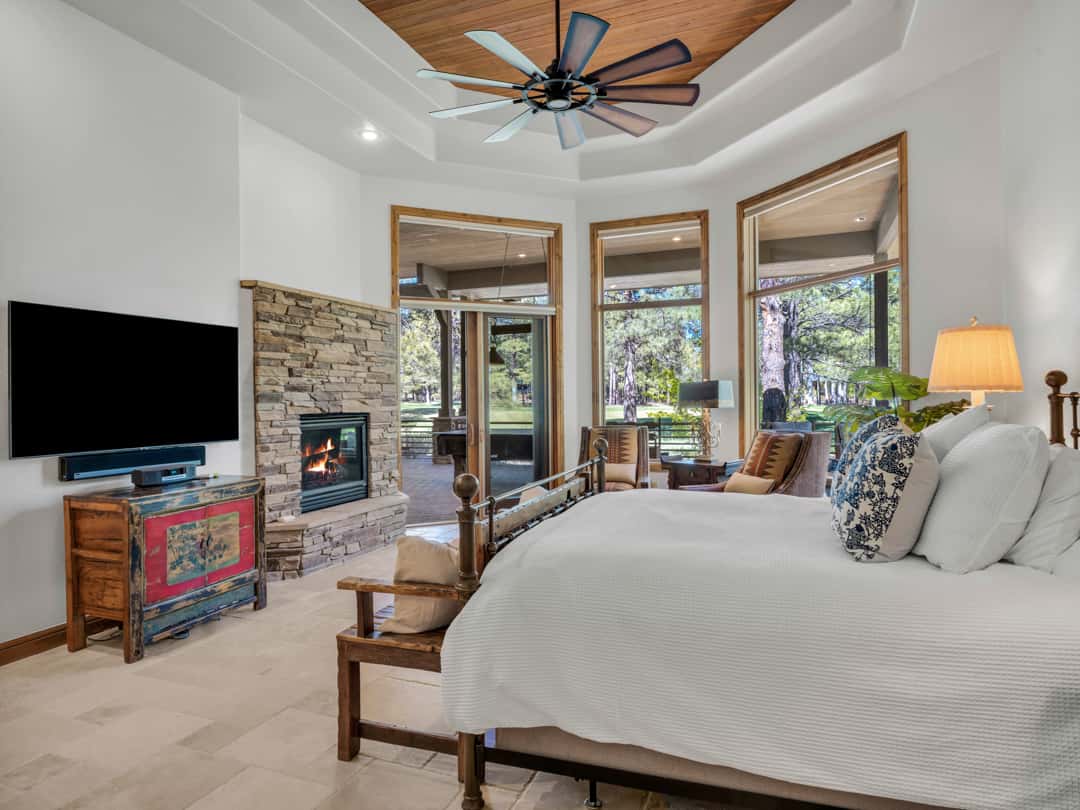 17 of 52. Luxury primary bedroom featuring a cozy stone fireplace, oversized windows, and beautiful golf course surroundings that create a private retreat experience.