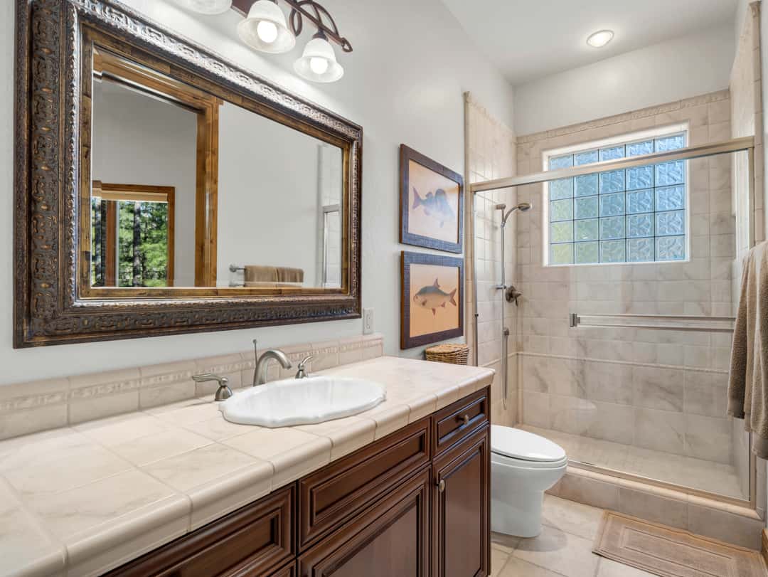 25 of 52. Beautiful guest bathroom featuring tiled shower surrounds, custom vanity cabinetry, elegant framed mirror, and upscale finishes throughout the space.