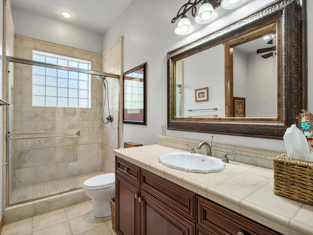 28 of 52. Stylish guest bath with walk-in shower, custom wood cabinetry, framed designer mirror, and refined tile finishes designed for comfort and functionality.
