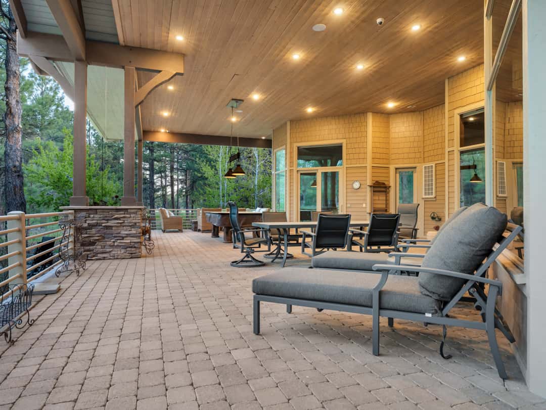 34 of 52. Huge covered patio designed for outdoor dining and entertaining, complete with custom pavers, forest views, and spacious seating throughout.