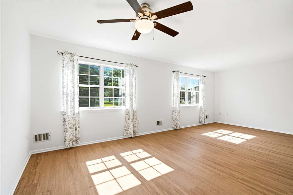 15 of 39. Bright, open living space featuring large windows and a ceiling fan, perfect for versatile furnishings.