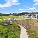 Scenic boardwalks weave through vibrant green spaces, leading to diverse shops and community areas.