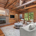 Cozy living space features exposed beams, a brick fireplace, and large windows for natural light.