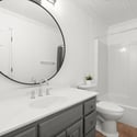 Bright and modern bathroom featuring a circular mirror, spacious vanity, and a sleek walk-in shower.