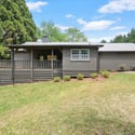 Welcoming home surrounded by lush greenery, featuring a spacious deck and inviting exterior design.