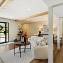 Warm and welcoming living room featuring exposed ceiling beams, wide plank floors, and oversized doors opening to lush outdoor views.