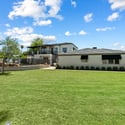 Wide-open grassy backyard ideal for gatherings, play, or relaxation, surrounded by mature trees and manicured landscaping.