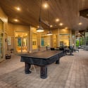 Massive covered patio designed for year-round entertaining with lounge seating, recreation space, wood ceilings, and beautiful views of the surrounding forest landscape.