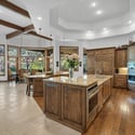 Open-concept great room with soaring ceilings, exposed wood beams, fireplace feature wall, and expansive windows overlooking scenic pine forest surroundings.