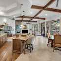Open-concept kitchen and dining area with exposed beams, large windows, custom wood cabinetry, and seamless connection to the surrounding pine forest views.
