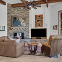 Inviting living room with floor-to-ceiling stone fireplace, custom built-ins, expansive windows, and comfortable seating areas overlooking the beautiful forest setting.