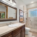 Beautiful guest bathroom featuring tiled shower surrounds, custom vanity cabinetry, elegant framed mirror, and upscale finishes throughout the space.