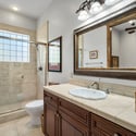 Stylish guest bath with walk-in shower, custom wood cabinetry, framed designer mirror, and refined tile finishes designed for comfort and functionality.