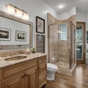 Upscale guest bath featuring tiled walk-in shower, granite countertops, custom vanity cabinetry, and elegant lighting for a refined luxury feel.
