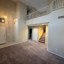 Dramatic vaulted ceilings and an open staircase create a striking focal point in this spacious living area. Natural light and neutral finishes provide a bright and welcoming environment.