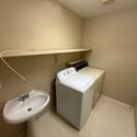 Dedicated laundry area featuring washer and dryer hookups, utility sink, and storage shelving. A practical space that adds convenience and efficiency to daily household tasks.