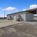 Rear exterior showcases additional workshop access, generous concrete work areas, covered storage, and room for trailers, RVs, equipment, or future outdoor improvements on this versatile property.