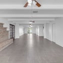 Expansive great room features updated tile flooring, ceiling fans, exposed beams, and a beautiful brick fireplace that anchors the spacious open floor plan, perfect for entertaining and everyday living.