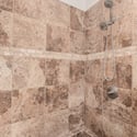 Floor-to-ceiling tiled walk-in shower with upgraded fixtures and decorative tile accents creates a luxurious spa-like atmosphere within the remodeled primary bathroom.