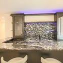 A stunning custom wet bar features granite countertops, beverage sink, glass cabinetry, designer backsplash, accent lighting, and bar seating perfect for entertaining guests.