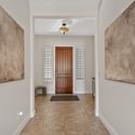 An inviting foyer showcases a custom wood front door, plantation shutters, tile flooring, and clean architectural lines that introduce the home's elegant and spacious interior.