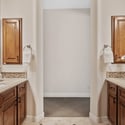 The spacious primary bathroom showcases dual vanities, custom wood cabinetry, stone countertops, decorative tile accents, and elegant finishes that create a luxurious everyday retreat.