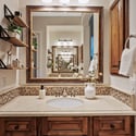 Designer lighting, custom cabinetry, stone countertops, decorative shelving, and an oversized framed mirror combine to create a sophisticated vanity space in the primary bathroom.