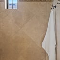 The walk-in shower features elegant floor-to-ceiling tile, decorative mosaic accents, natural lighting, and spacious proportions for a spa-like bathing experience.