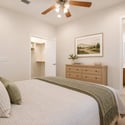 The staged primary bedroom highlights generous proportions, plush carpeting, ceiling fan, walk-in closet access, and an adjoining private bathroom for everyday comfort and convenience.