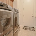 Designed for convenience, this laundry room includes front-loading appliances, built-in cabinetry, utility sink, tile flooring, and extra workspace for everyday household tasks.