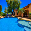 A resort-inspired backyard showcases a custom swimming pool with waterfall, elevated spa, tropical landscaping, mature trees, and covered patio for exceptional outdoor living.