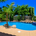 Enjoy a peaceful backyard retreat with a sparkling pool, raised spa, mature palms, decorative rock accents, and lush landscaping designed for relaxing and entertaining.