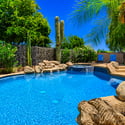 Beautiful landscaping surrounds the custom swimming pool and spa, creating a private backyard oasis with tropical plants, decorative boulders, and multiple spaces for outdoor enjoyment.