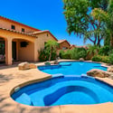 A beautiful perspective of the custom swimming pool showcases the elevated spa, natural rock features, mature palms, covered patio, and professionally landscaped outdoor living space.