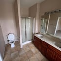 The primary bathroom features a large dual-sink vanity, expansive mirror, walk-in shower, and durable tile flooring, providing both comfort and functionality.