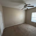 This inviting bedroom features soft carpeting, natural light, ceiling fan, and a roomy closet, providing comfortable accommodations and versatile functionality within the home.