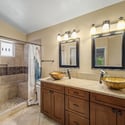 The beautifully updated bathroom showcases dual vessel sinks, granite countertops, custom wood cabinetry, elegant fixtures, and a spacious tiled walk-in shower that adds everyday luxury.