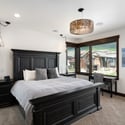 Luxurious primary bedroom featuring a stunning stone fireplace and modern lighting, a five-piece en suite bath, mountain views, and a private balcony.