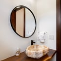 This unique bathroom features a natural stone sink and a modern circular mirror, enhancing its distinctive design.