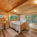 Cozy bedroom with wood paneling, large windows showcasing natural light, and a framed view of Black Butte and Mt. Jefferson.