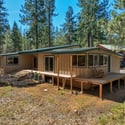 Spacious home nestled among tall pines, featuring ample outdoor space and a welcoming deck that wraps from the great room to the second bedroom, around to the primary suite.