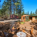 This peaceful retreat features outdoor seating around a cozy fire pit, surrounded by towering pines and a spacious yard.