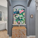 Bright entryway featuring a colorful artwork and an eye-catching patterned console table, leading to a spacious bathroom.
