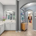Spacious bathroom with double sinks, modern lighting, and an inviting pathway to a well-organized closet.
