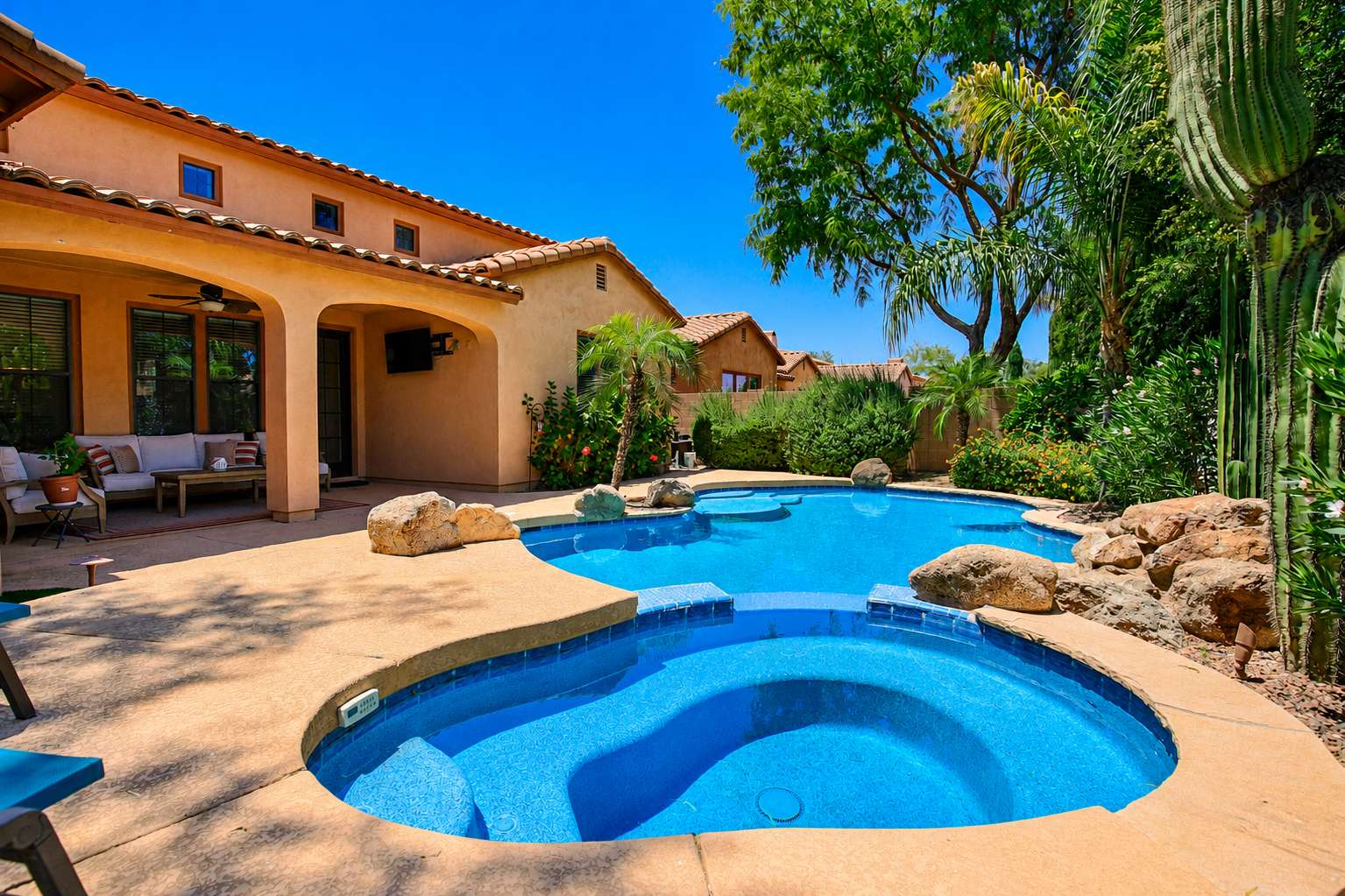 62 of 72. A beautiful perspective of the custom swimming pool showcases the elevated spa, natural rock features, mature palms, covered patio, and professionally landscaped outdoor living space.