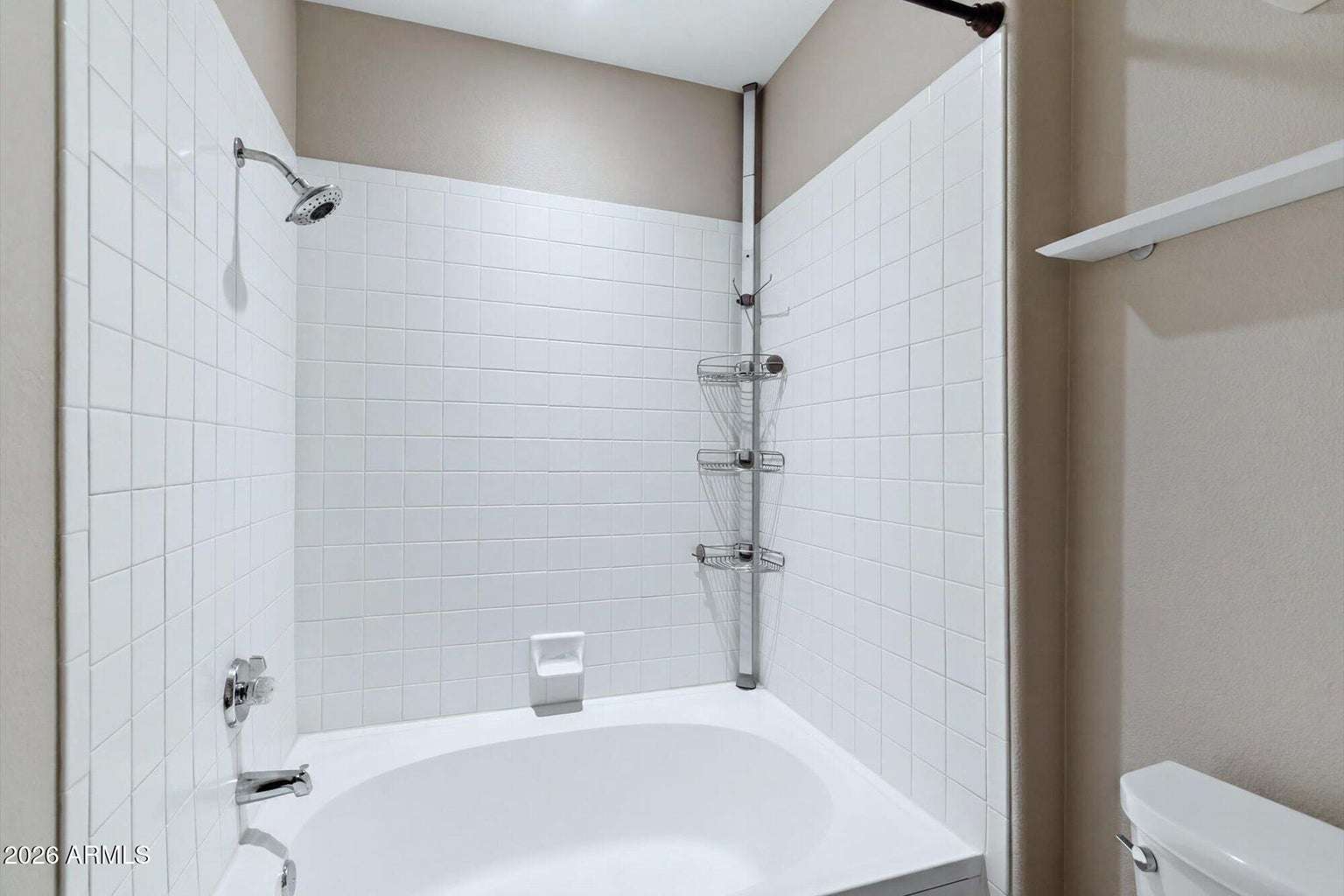 21 of 32. The bathroom features a full tub and shower combination with clean tile surrounds, convenient shelving, and neutral finishes that create a bright, functional space for everyday comfort.