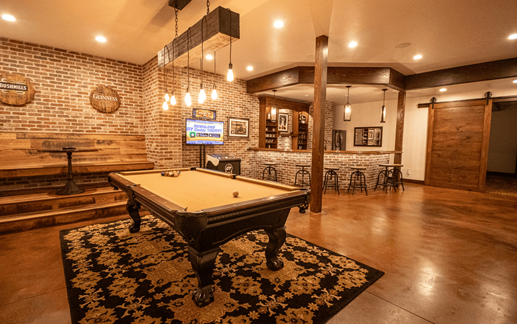 26 of 42. Discover a vibrant game room featuring a pool table, game console, bar, and rustic brick accents for entertainment.