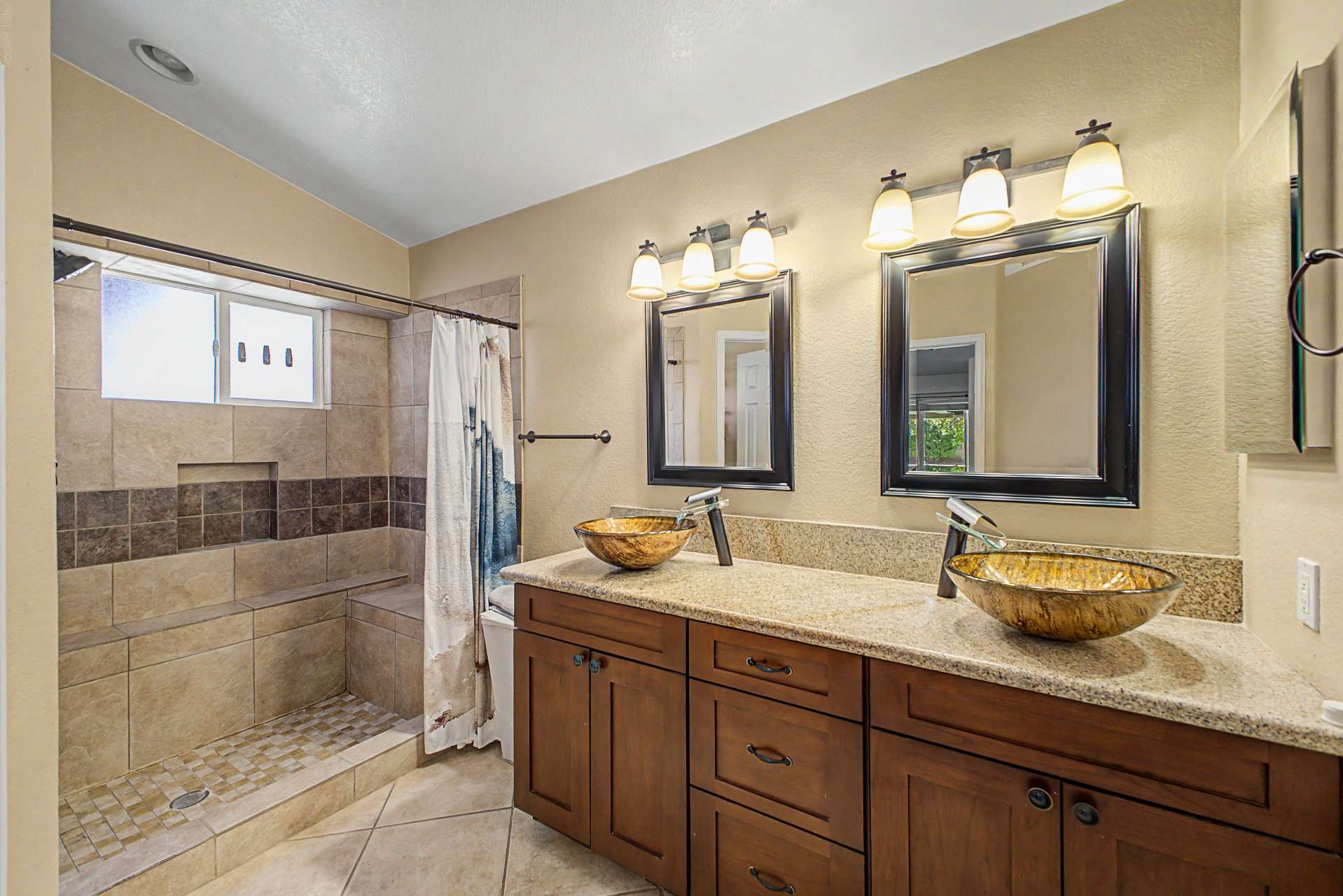 32 of 47. The beautifully updated bathroom showcases dual vessel sinks, granite countertops, custom wood cabinetry, elegant fixtures, and a spacious tiled walk-in shower that adds everyday luxury.
